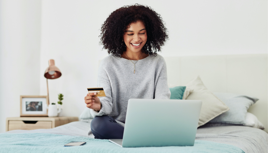 Young woman sitting on bed looking at online deals with laptop